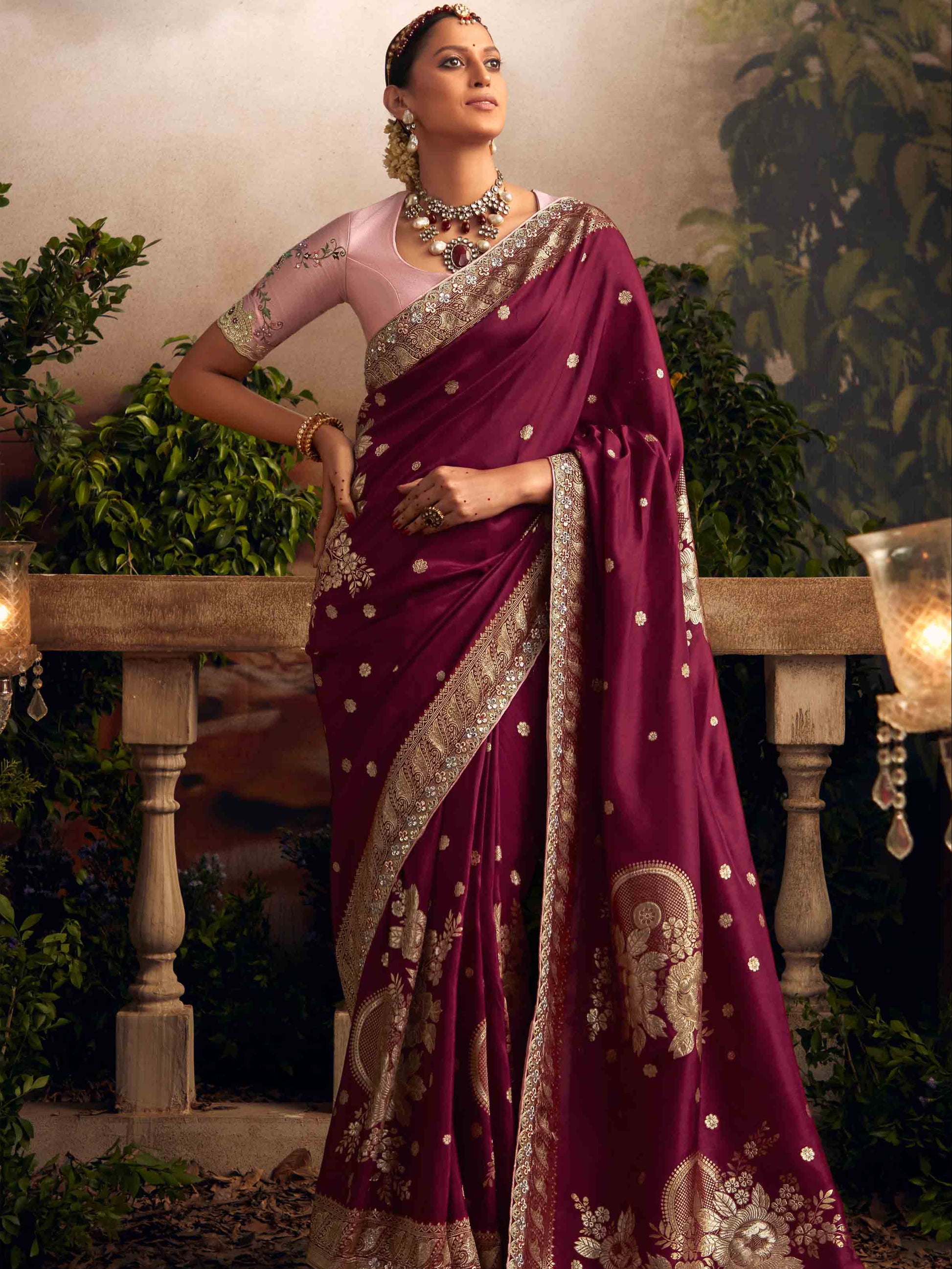 Woman in a maroon saree with gold embroidery standing outdoors, with 'Sindhuri' branding visible.