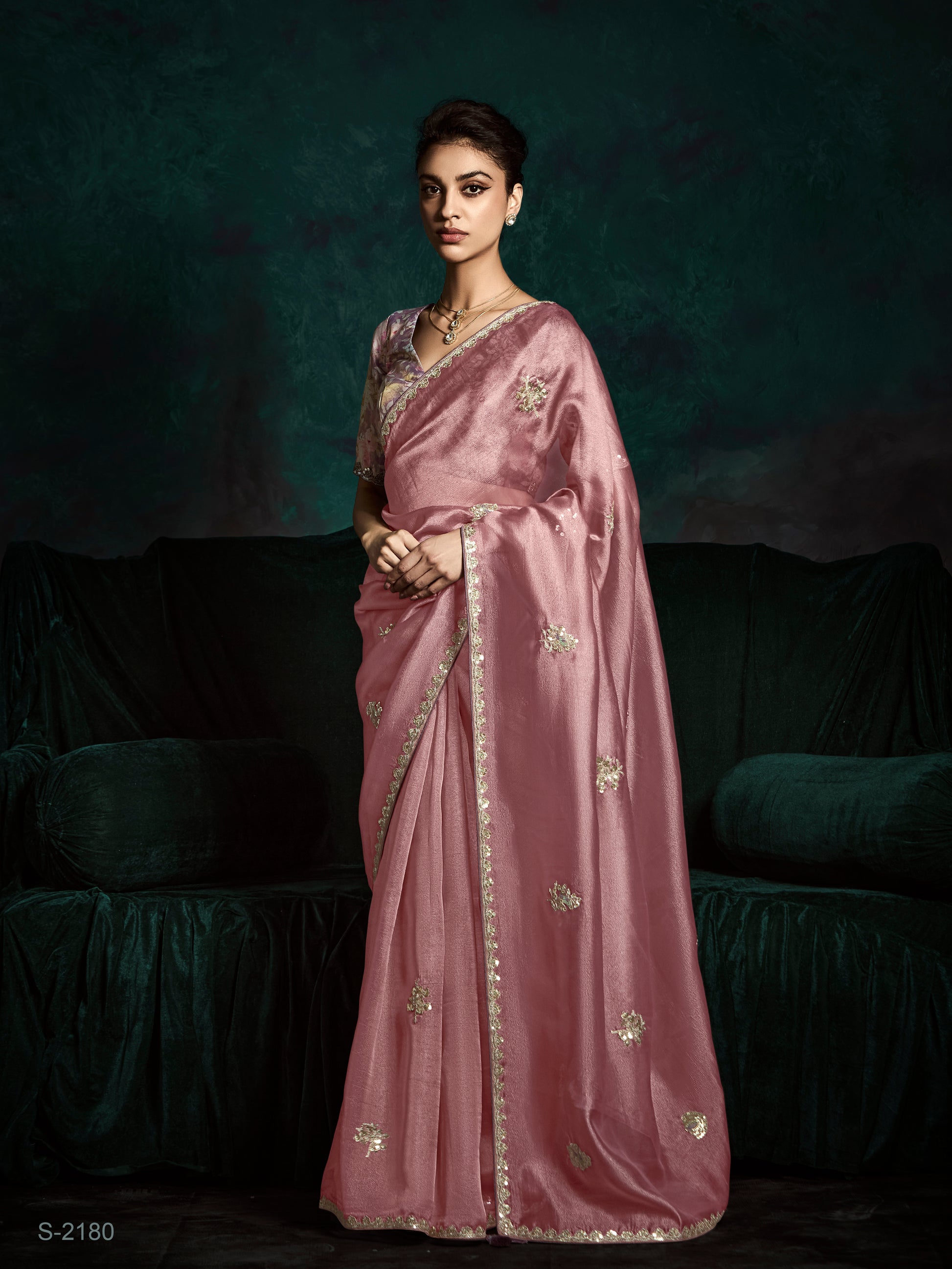 Woman wearing a pink saree with gold patterns against a dark background