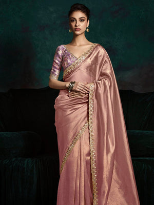 Woman wearing a pink saree with gold border against a dark background