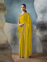 Woman wearing a yellow saree with gold border against a textured wall background