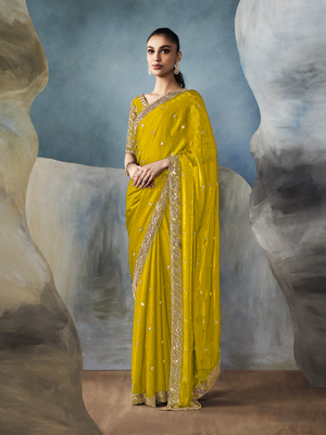 Woman wearing a yellow saree with gold border against a textured wall background