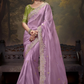 Woman wearing a lavender saree with green blouse against a decorative backdrop