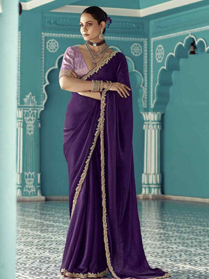 Woman in a purple saree with gold border standing in a decorative room.