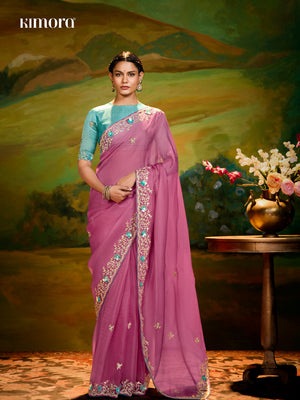 Woman in a pink saree with a decorative border against a painted landscape background