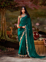 Woman in a teal saree with floral patterns standing in a scenic background