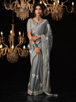 Woman in a silver saree standing in front of chandeliers on a black background