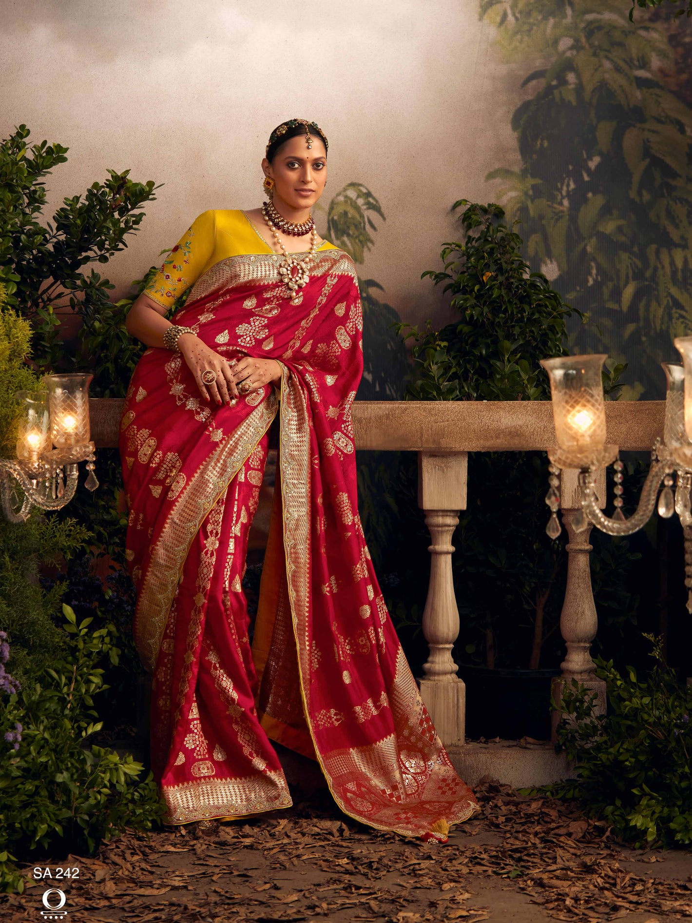 Woman in a red and yellow saree with jewelry standing in a decorated outdoor setting.