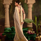 Woman in a white saree standing in a decorated indoor setting with floral arrangements.
