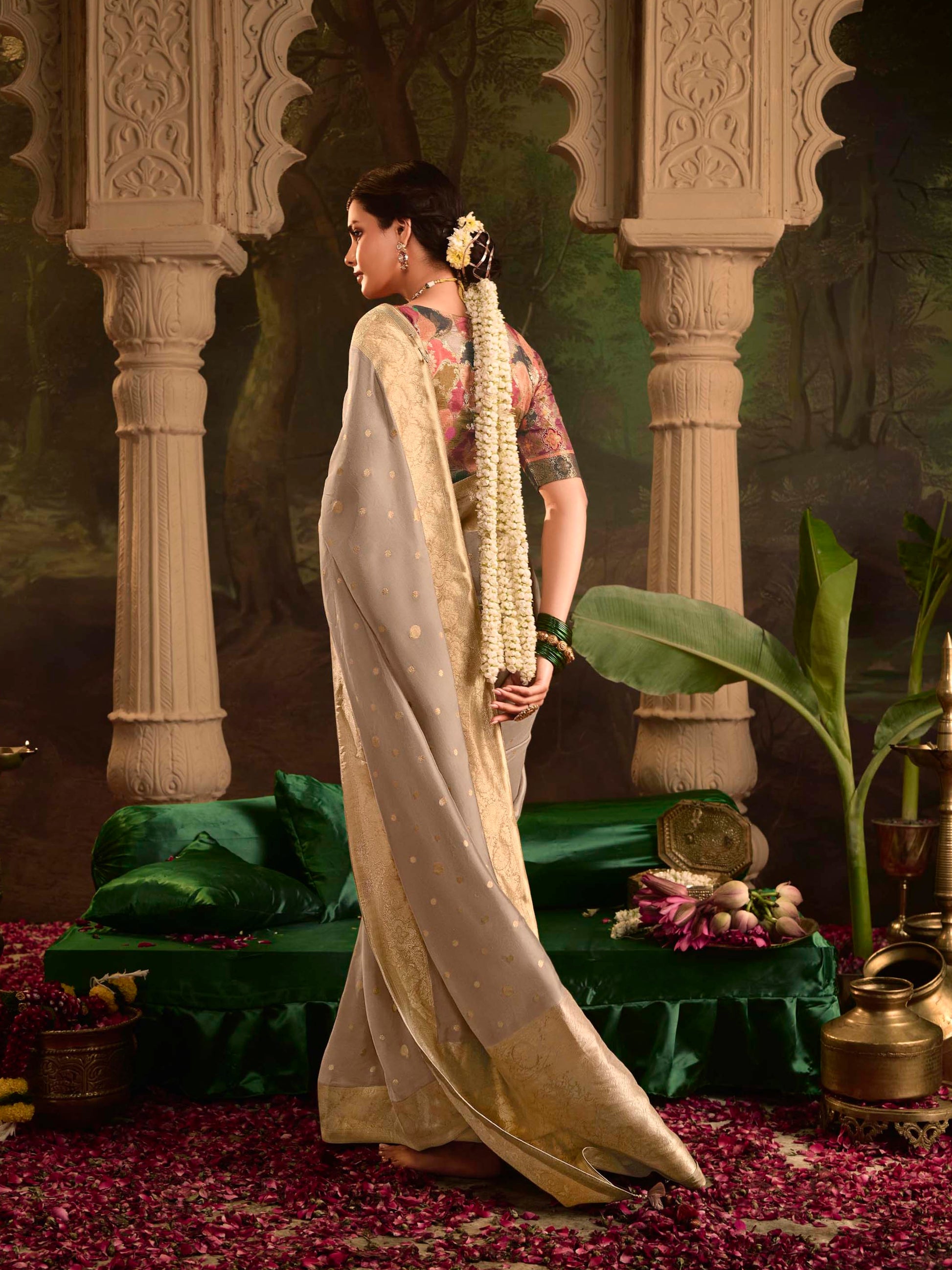 Woman in a white saree standing in a decorated indoor setting with floral arrangements.