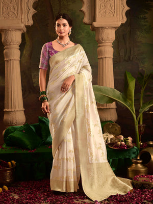 Woman in a white saree with a purple blouse standing in an ornate setting.