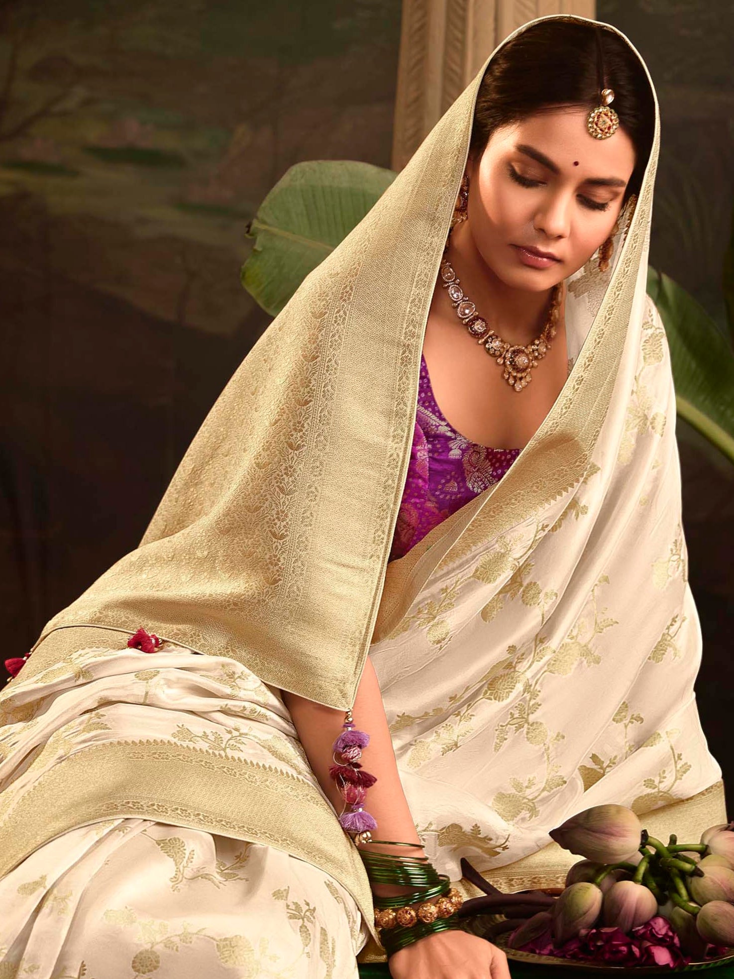 Woman in a white saree with a plant and traditional lamp in the background