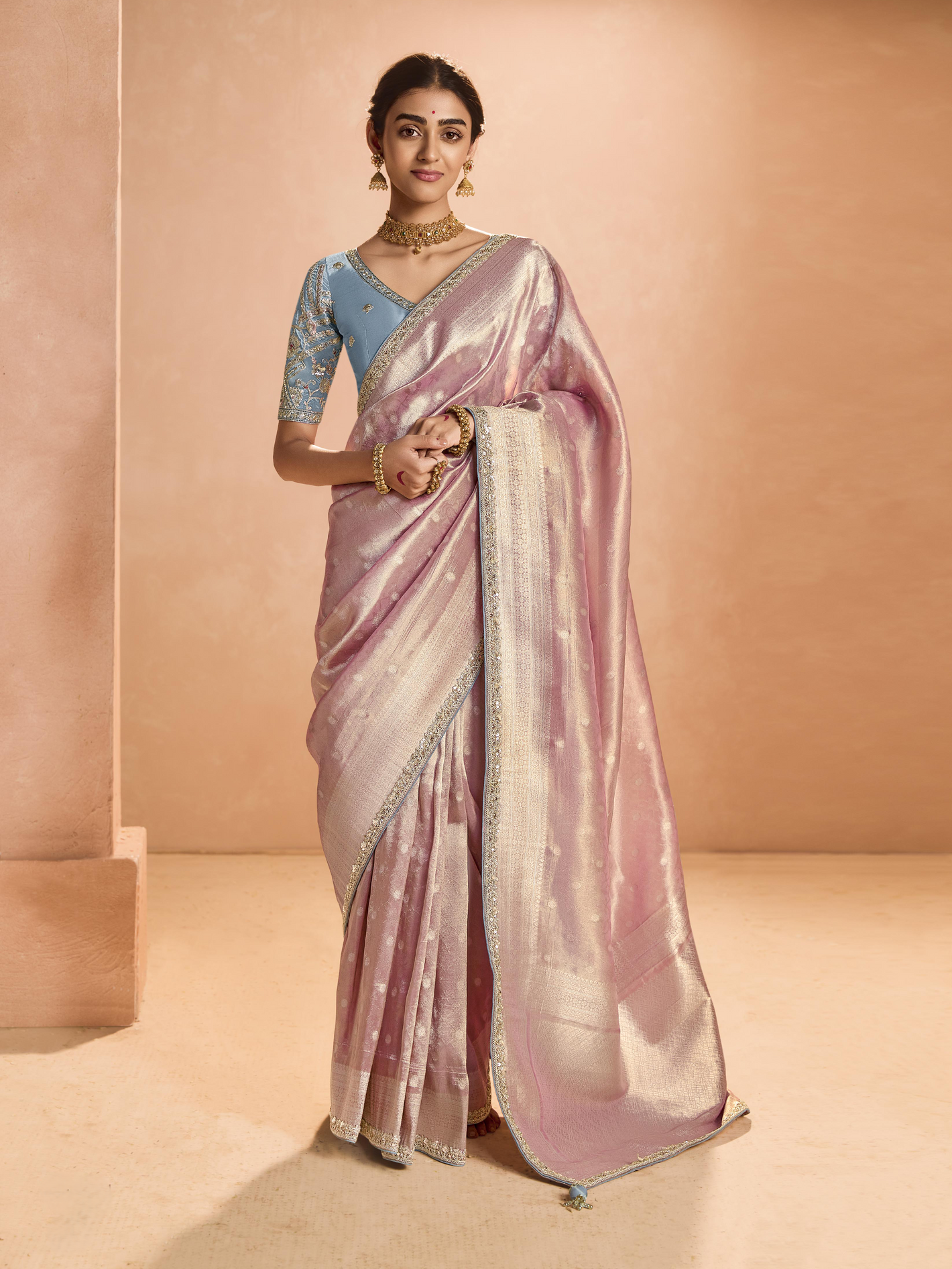Woman wearing a pink saree with a blue blouse against a beige background